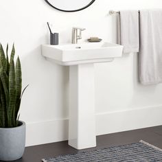 a white sink sitting under a round mirror next to a potted plant and rug