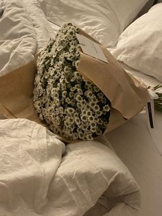 an unmade bed with white linens and flowers on the pillow, along with a brown paper bag