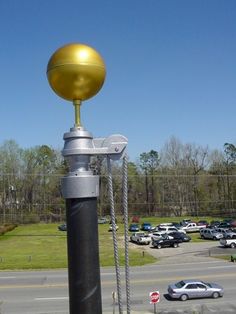 a pole with a golden ball on top in front of a parking lot filled with cars