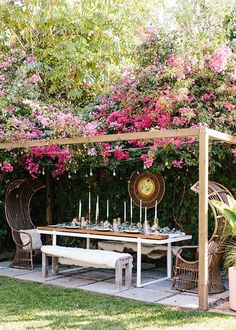 an outdoor dining area with wicker furniture and pink flowers on the wall behind it