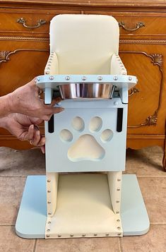 a person holding a dog's food bowl in front of a wooden dresser