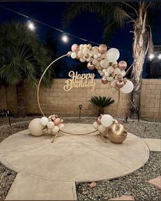 a happy birthday sign with balloons on it in the middle of a courtyard at night