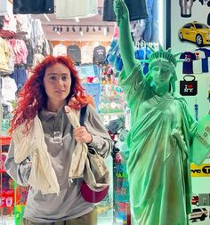 a woman with red hair standing in front of a statue of liberty and looking at the camera