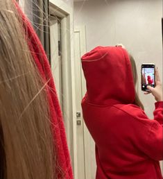 a person in a red hoodie taking a selfie with a cell phone while standing in front of a mirror