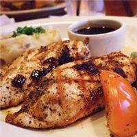 a white plate topped with chicken, potatoes and carrots next to a cup of sauce