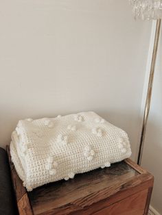 a white crocheted blanket sitting on top of a wooden table next to a lamp