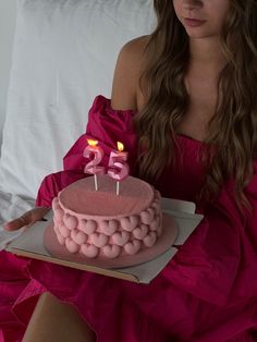 a woman in a pink dress holding a cake with two candles on it and the number twenty five