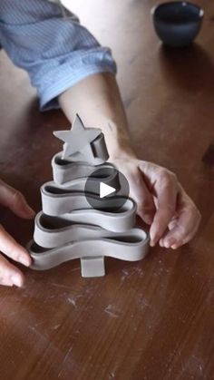 a person is holding a christmas tree made out of paper and scissors on a wooden table