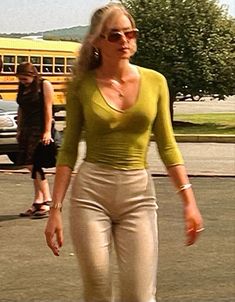 a woman walking across a parking lot next to a school bus