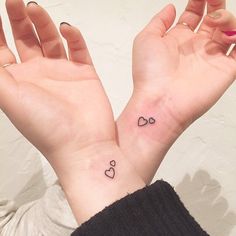 two hands with small tattoos on them, one has a heart and the other has a bow