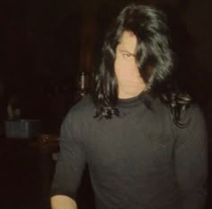 a man with long hair standing in the dark