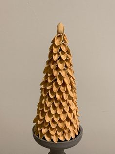 a small wooden pine cone on top of a black pedestal in front of a gray wall