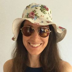 a woman wearing sunglasses and a hat with flowers on it, smiling at the camera