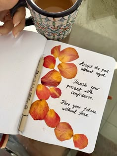 a person holding a cup of coffee and an open notebook with flowers on it next to a pen