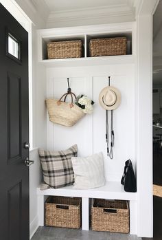 a white bench with baskets and hats hanging on the wall next to two black doors