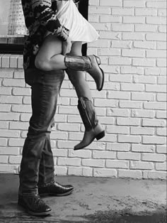 black and white photograph of a man carrying a woman on his back in front of a brick wall