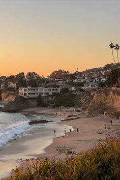 people walking on the beach at sunset with houses in the background and trees to the side