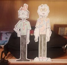 two paper cutouts of people standing next to each other in front of a bag