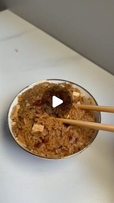 two wooden chopsticks sticking out of a bowl filled with rice and other food