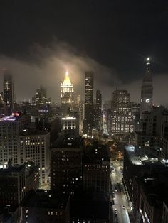 the city skyline is lit up at night with lights and clouds in the sky above