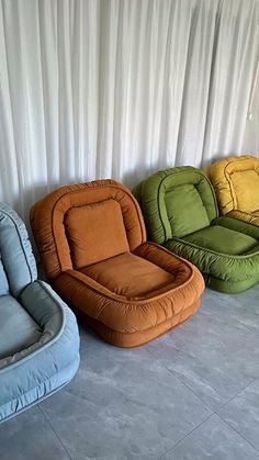 four different colored bean bag chairs lined up against a white wall with drapes behind them