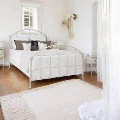 a white bed sitting in a bedroom on top of a hard wood floor next to a window