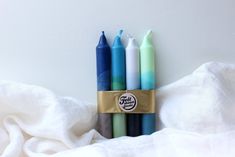 four different colored candles sitting next to each other on a white sheet with a gold ribbon