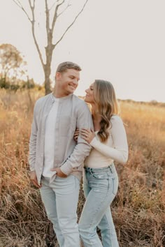 an engaged couple standing in the middle of a field