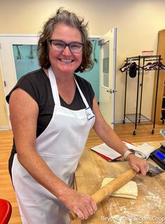 a woman in an apron is making bread on a wooden table with a rolling pin