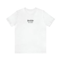 "Introducing our exceptional Bride t-shirt, the epitome of style and sophistication for your big day. Immerse yourself in unparalleled elegance with this meticulously crafted garment, meticulously designed to showcase your role as the Bride. Made from premium-quality materials, our t-shirt offers unmatched comfort and a flawless fit. The word \"Bride\" is intricately printed on the shirt, adding a touch of distinction to your wedding ensemble. With its exceptional craftsmanship and attention to White Bridal T-shirt With Short Sleeves, Classic Short Sleeve Tops For Wedding, Classic White Wedding Tops, Classic White Wedding Top, White Short Sleeve Bride T-shirt, Bride's White Short Sleeve T-shirt, White T-shirt For Bridal Shower Short Sleeve, White Short Sleeve T-shirt For Bridal Shower, Cotton Short Sleeve Wedding Shirt