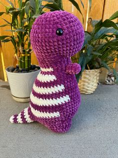 a purple stuffed animal sitting next to a potted plant