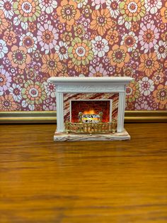 a small white fireplace sitting on top of a wooden floor next to a wall with flowers