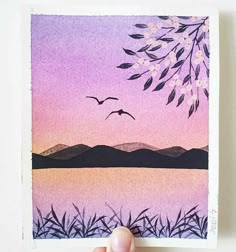 a hand holding up a card with watercolors on it and birds flying in the sky