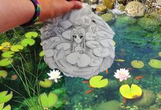 a drawing of a woman is being held up over a pond with lily pads and water lilies