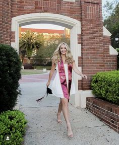 a woman in a pink and white graduation gown is holding her hand out as she walks towards the camera