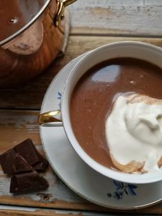 a cup of hot chocolate with whipped cream on top and some pieces of chocolate next to it