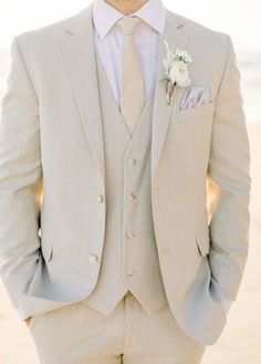 a man in a gray suit and white flower boutonniere is standing on the beach