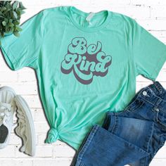 a t - shirt with the words be kind on it next to jeans and sneakers