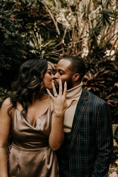 a man and woman standing next to each other in front of trees with their fingers up