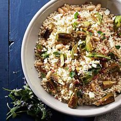 a white bowl filled with rice and vegetables on top of a blue wooden table next to a spoon