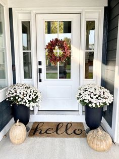 two large black vases with white flowers sit on the front porch of a house