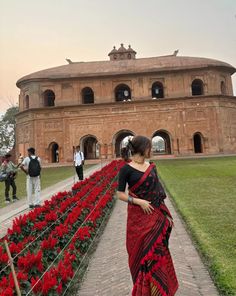 a woman in a red and black sari walking by some flowers