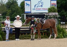 two women standing next to a brown horse holding a white plate in front of them