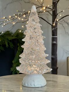 a glass christmas tree sitting on top of a table next to a tree with lights