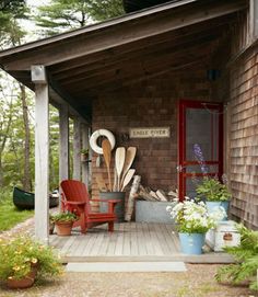 a porch with chairs and potted plants on the front steps, next to a red door