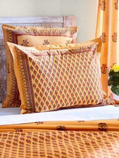 a bed with yellow and brown pillows on it's sides, next to a window