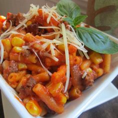 a white bowl filled with pasta and meat covered in sauce, parmesan cheese and basil