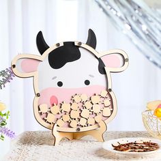 a cow with flowers in its mouth on a table next to a plate and vase