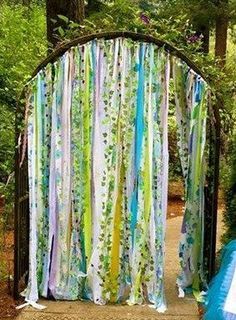 an outdoor wedding ceremony in the woods with colorful drapes hanging from it's gates