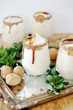 three glasses filled with white liquid sitting on top of a tray next to nuts and greenery